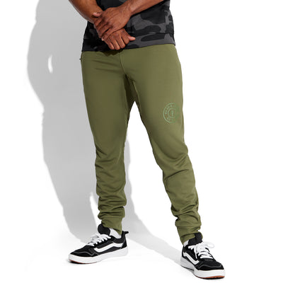 photo of male model wearing train jogger in olive. large golds gym weight plate logo above left knee in dark green