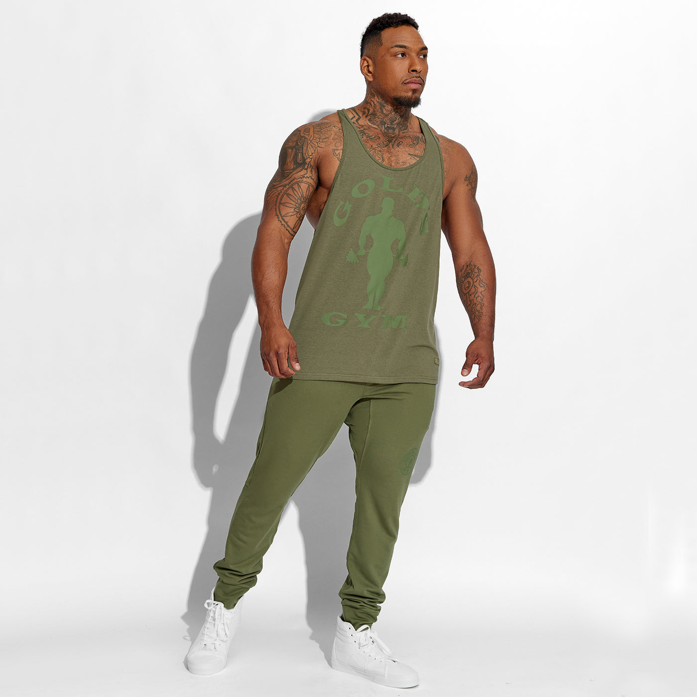 photo of male model wearing train stringer tank in olive. large solid muscle joe logo on front in green. golds gym surrounding also in green.