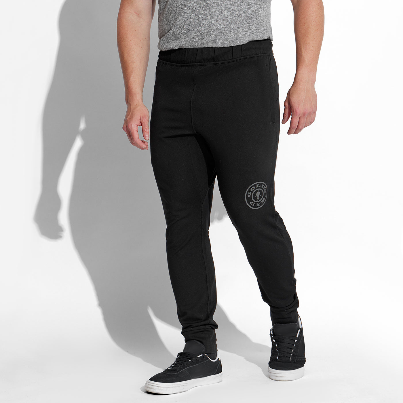 photo of male model wearing train jogger in black. large golds gym weight plate logo above left knee in grey