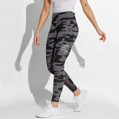 photo of female model wearing train high waist legging in black camo. large golds gym weight plate logo in white on left leg in middle below pocket