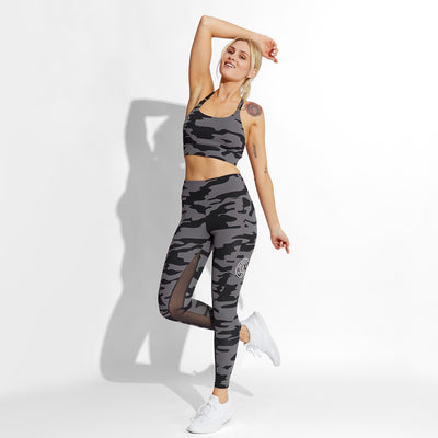 photo of female model wearing train high waist legging in black camo. large golds gym weight plate logo in white on left leg in middle below pocket.